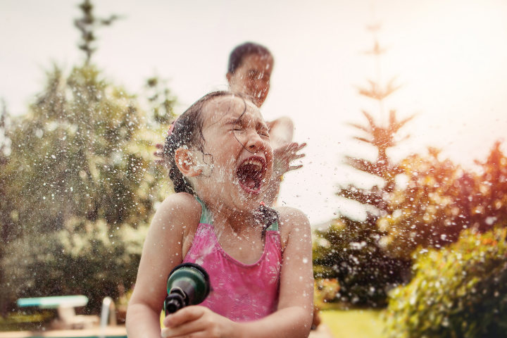 Mädchen im Badeanzug spritzt sich im Freien selbst mit dem Wasserschlauch nass