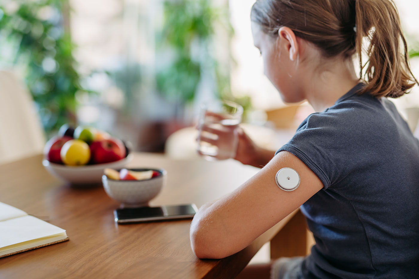 Mädchen mit Diabetes Sensor sitzt am Tisch und trinkt etwas