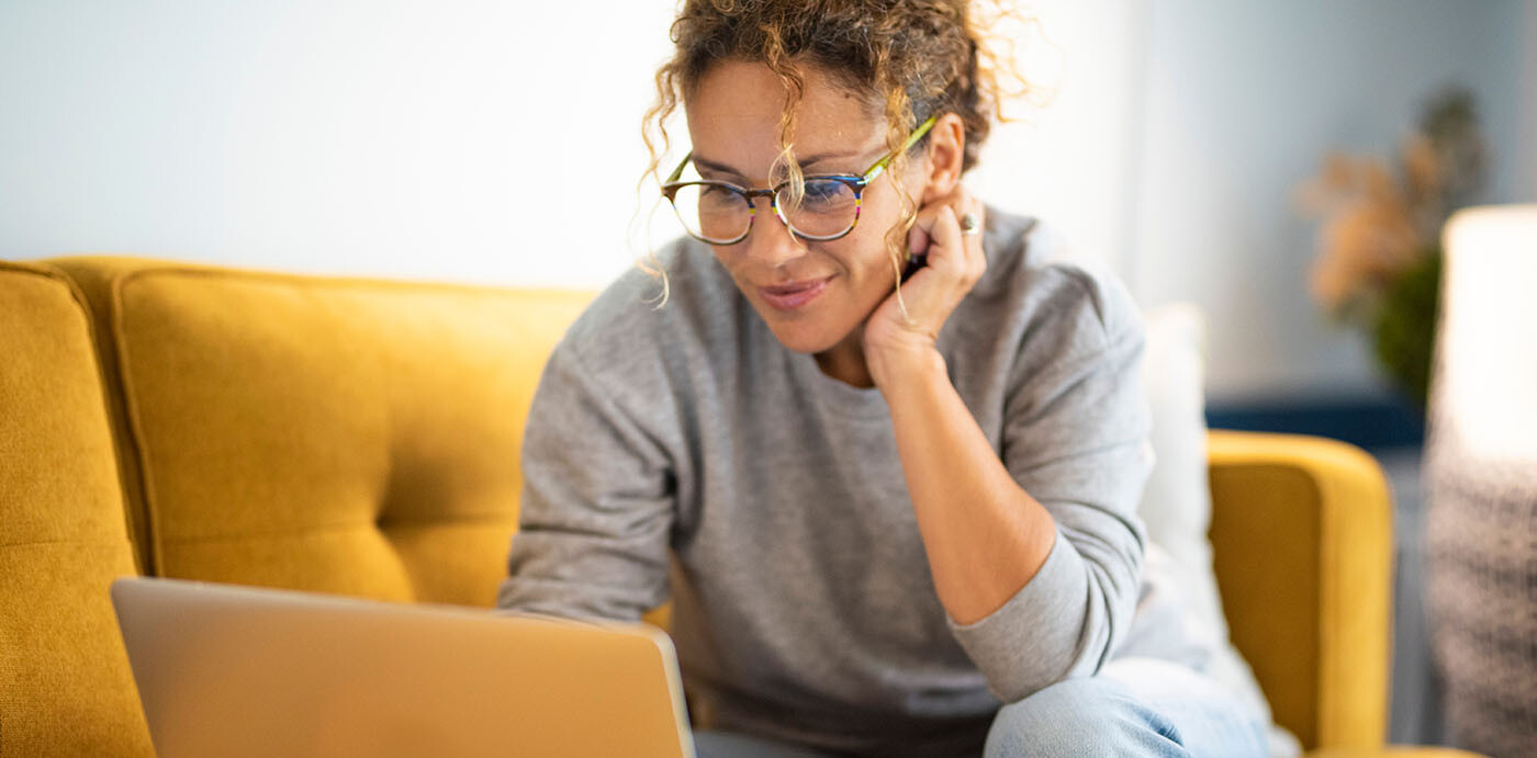 Frau, die auf einer Couch am Laptop sitzt und die Mitgliedschaftserklärung der BAHN-BKK ausfüllt