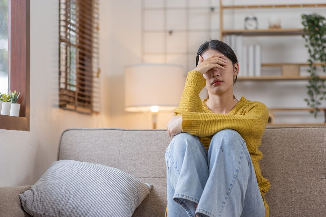 Eine Frau sitzt auf einem Sofa und hällt eine Hand über die Augen