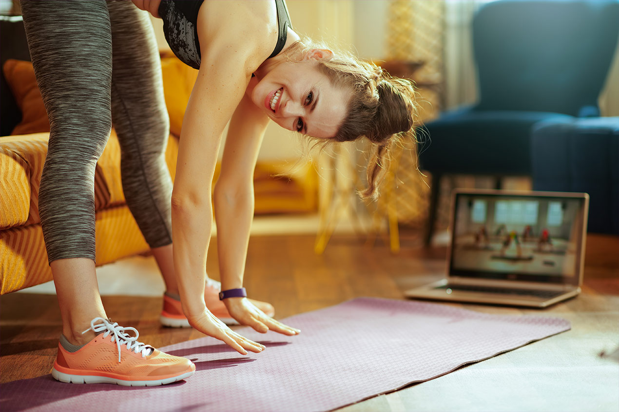 Eine Frau die stehend vorgebeut vor dem Computer Gymnastik mit einem Onlinekurs macht.