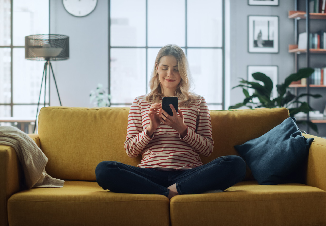 Frau sitzt auf gelbem Sofa und bedient ihr Smartphone