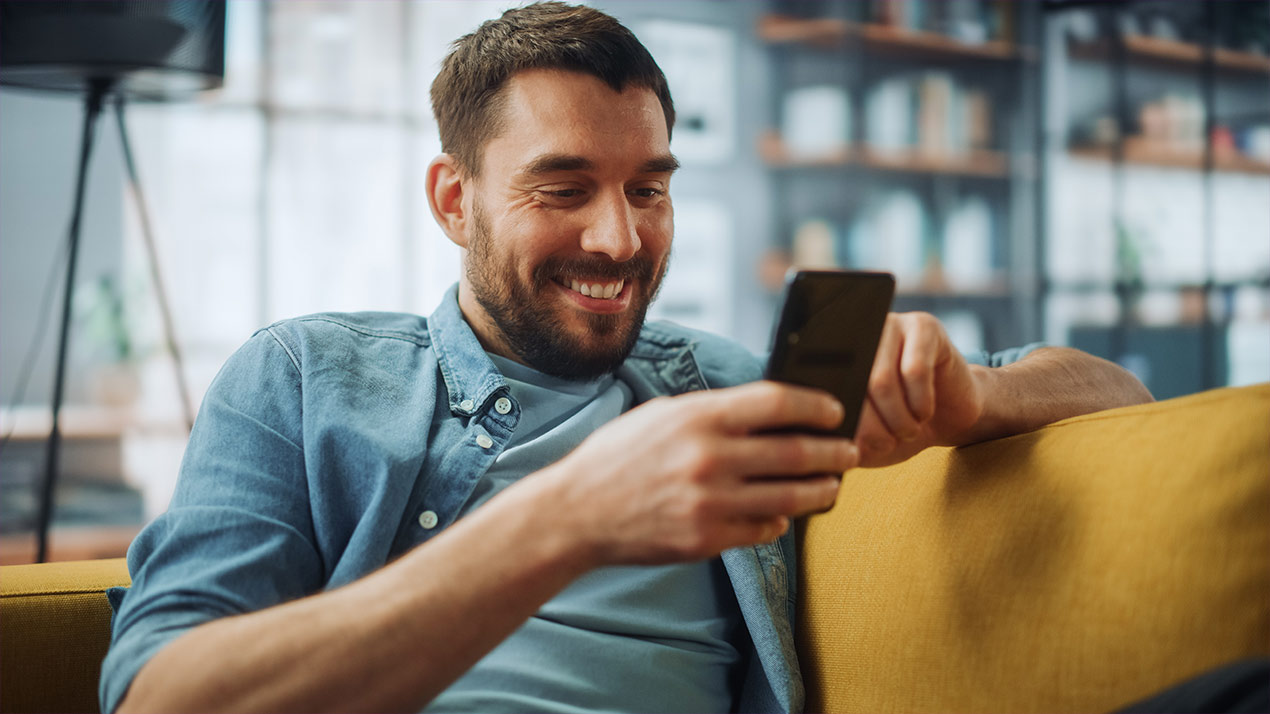 Mann sitzt auf Sofa und surft mit dem Handy.