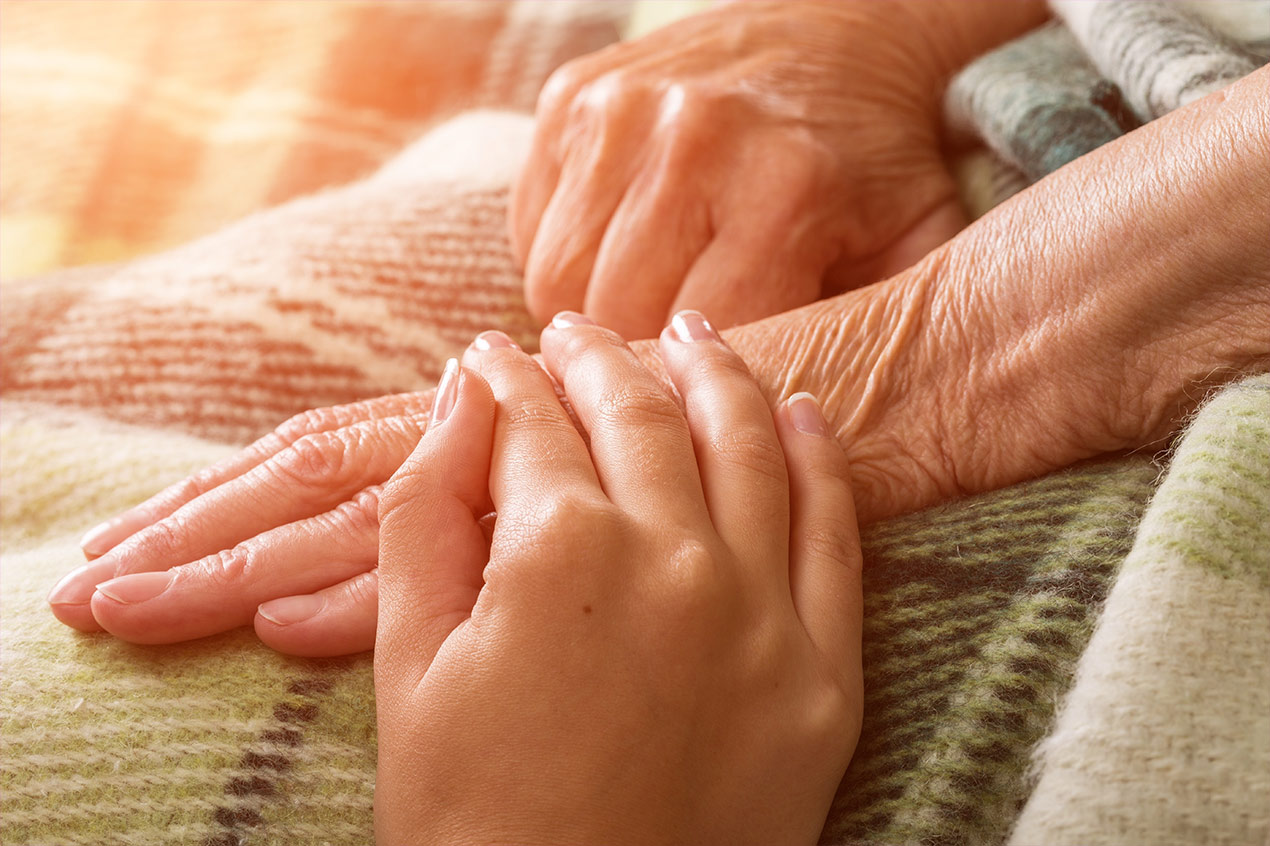 Junge Hand die eine alte Hand im Hospiz hält