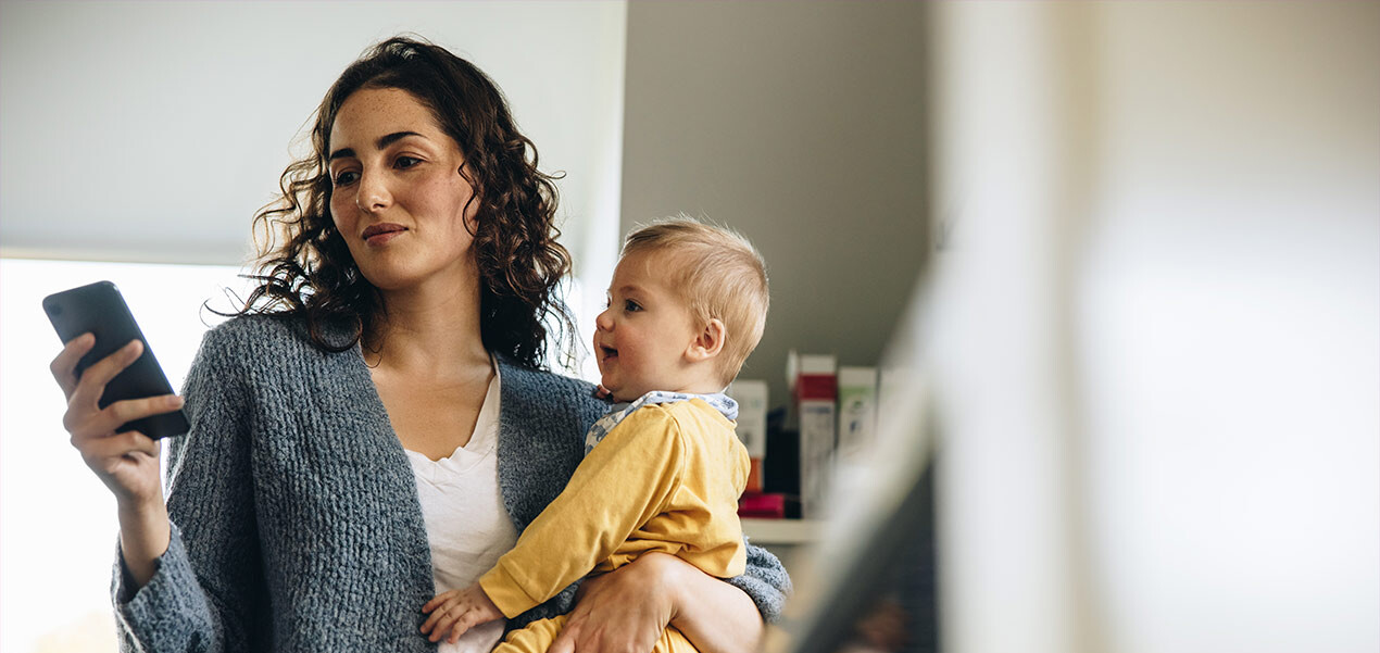 Eine Mutter mit ihrem Baby auf dem Arm wählt eine Telefonnummer