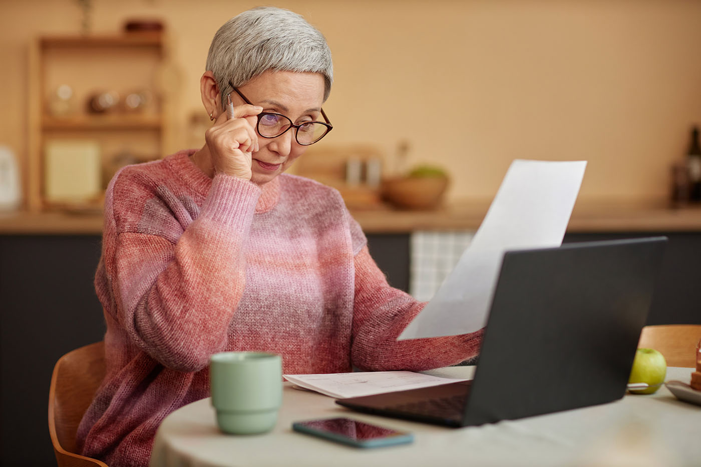 Ältere Frau, die vorm Laptop sitzt und ein Schreiben durchliest