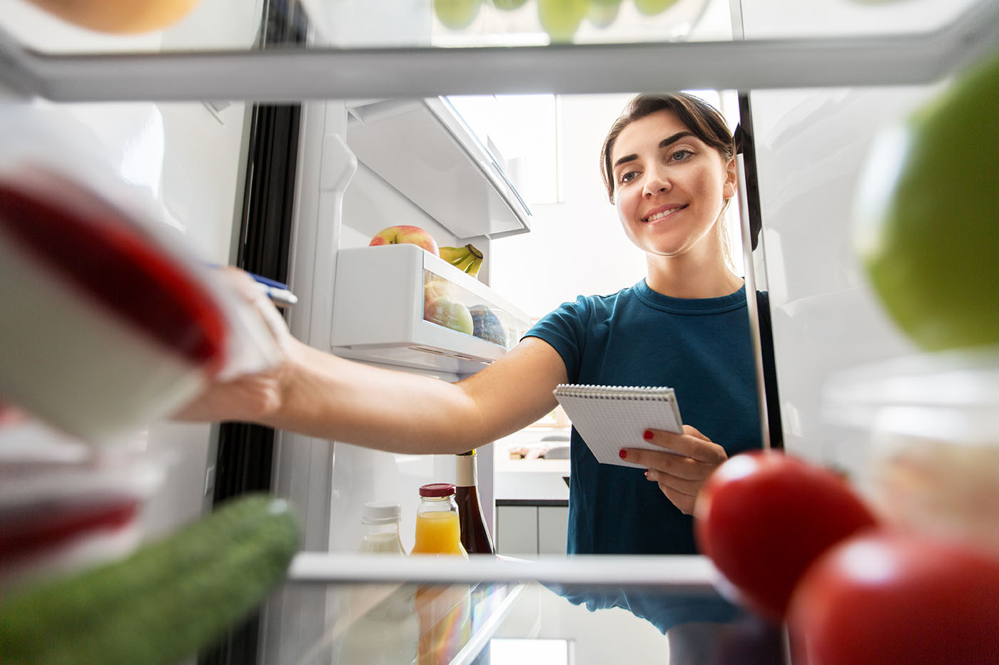 Frau, die mit einem Block in der Hand in den Kühlschrank schaut