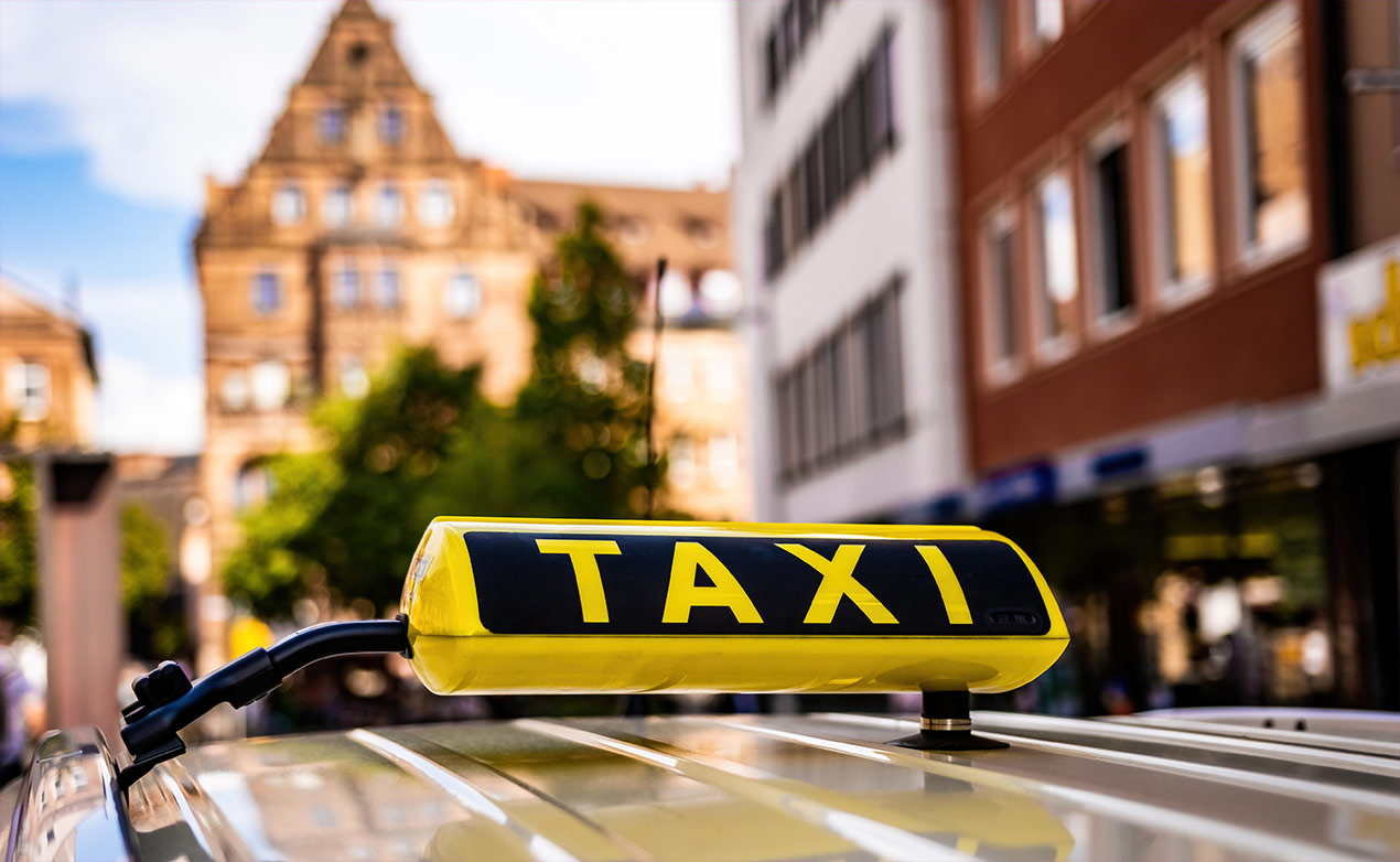 Ein Taxi. Nahaufnahme des Taxidaches vor einer verschwommenen Stadtkulisse.