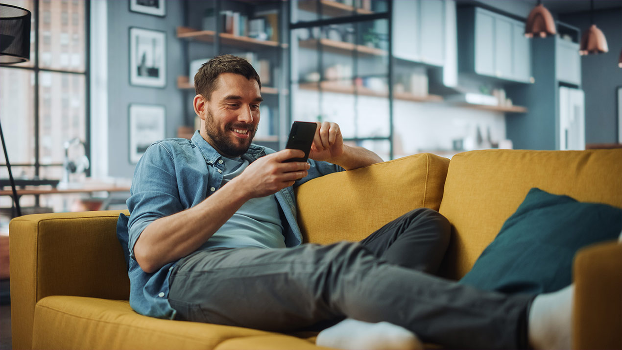 Mann sitzt auf einem gelben Sofa und schaut auf sein Handy.