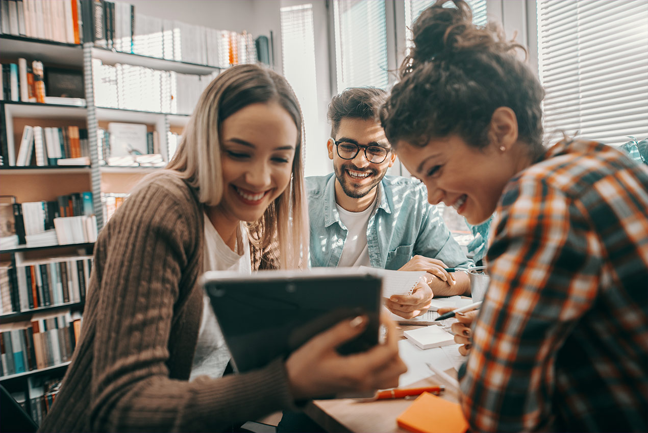 Drei Studentenenten in einer Bibliothek schauen auf ein Pad.