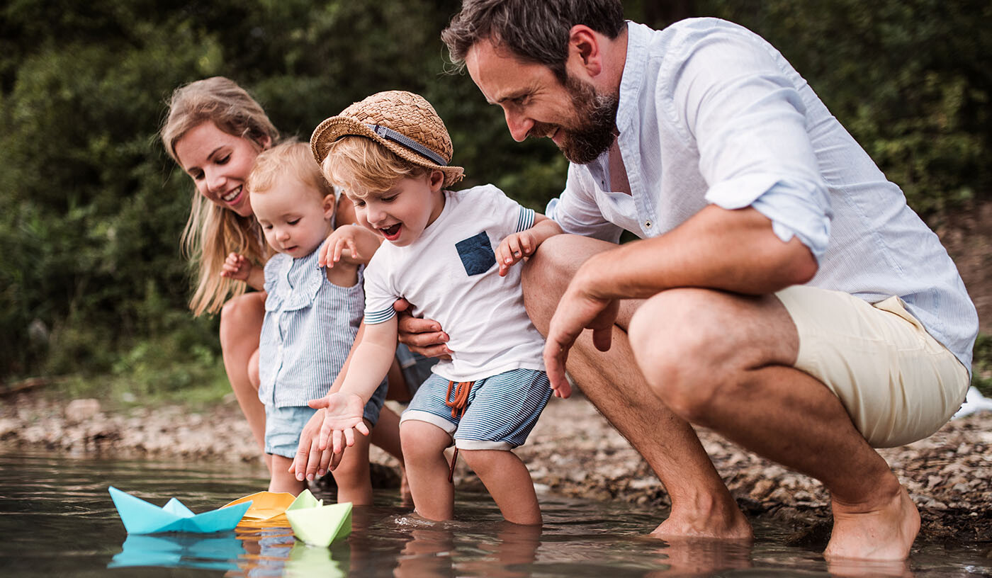 Junge Familie, die Papierboote am Seeufer schwimmen lassen