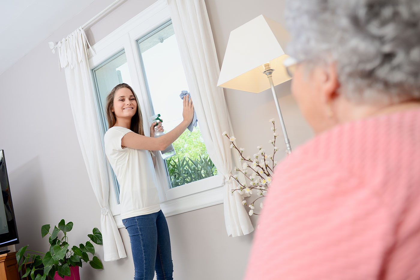 Eine Haushaltshilfe putzt bei einer Seniorin die Fenster