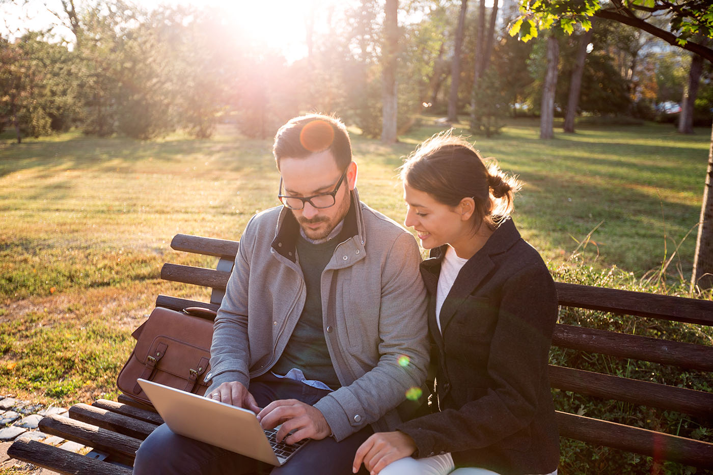 Mann und Frau sitzen auf einer Parkbahn und schauen auf einen Laptop