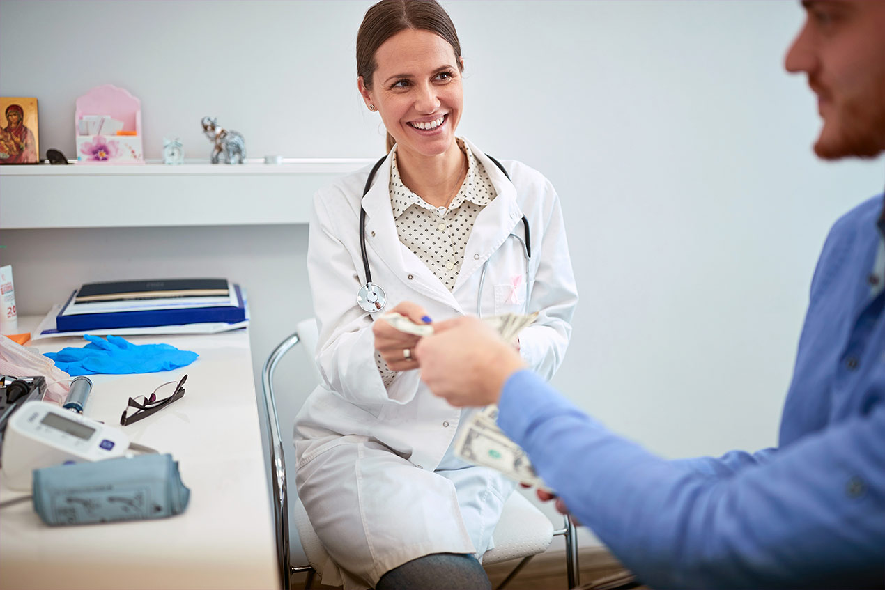 Ein Patient bezahlt bei einer Ärztin eine Behandlung.