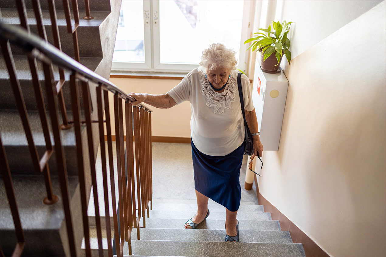 Eine Seniorin steigt im Treppenhaus die Treppe hoch