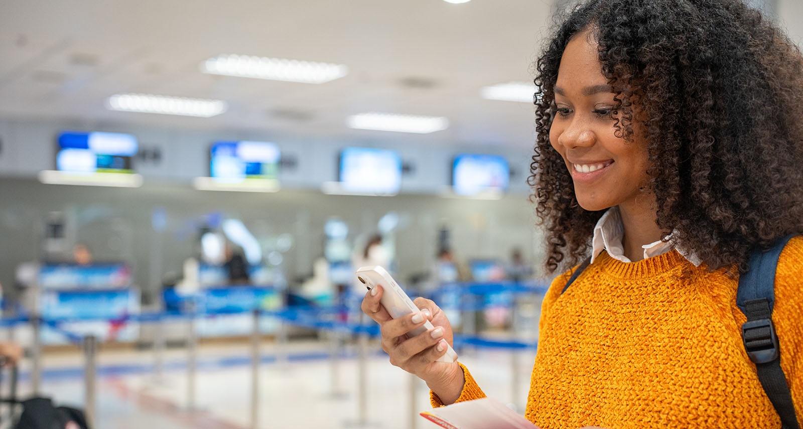 Junge Frau am Flughafen, die lächelnd auf ihr Smartphone schaut