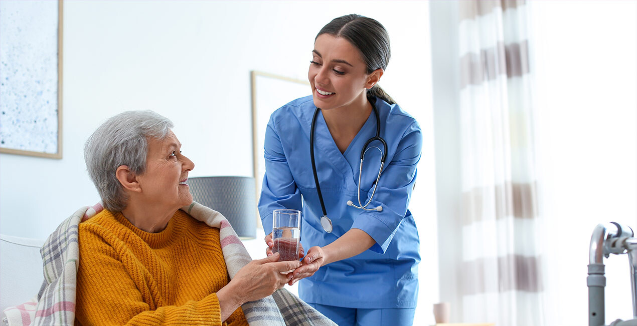 Eine Pflegerin bringt einer Seniorin etwas zu trinken