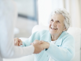 Lachende Alte Frau reicht Pflegekraft die Hände