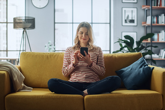Frau sitzt mit Smartphone auf dem Sofa